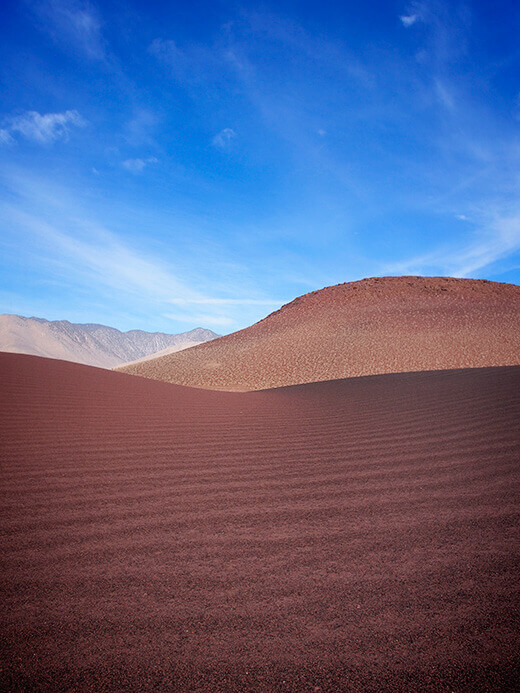 Mounds of red, brown, and black volcanic flakes form a sand-like texture