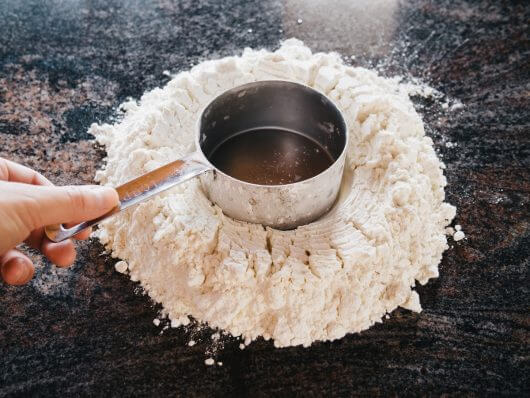 Mark a large well in the mound of flour