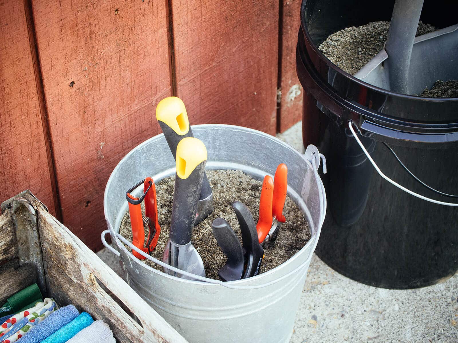 Small garden tools and shovel stored in "quick clean" buckets filled with oily sand