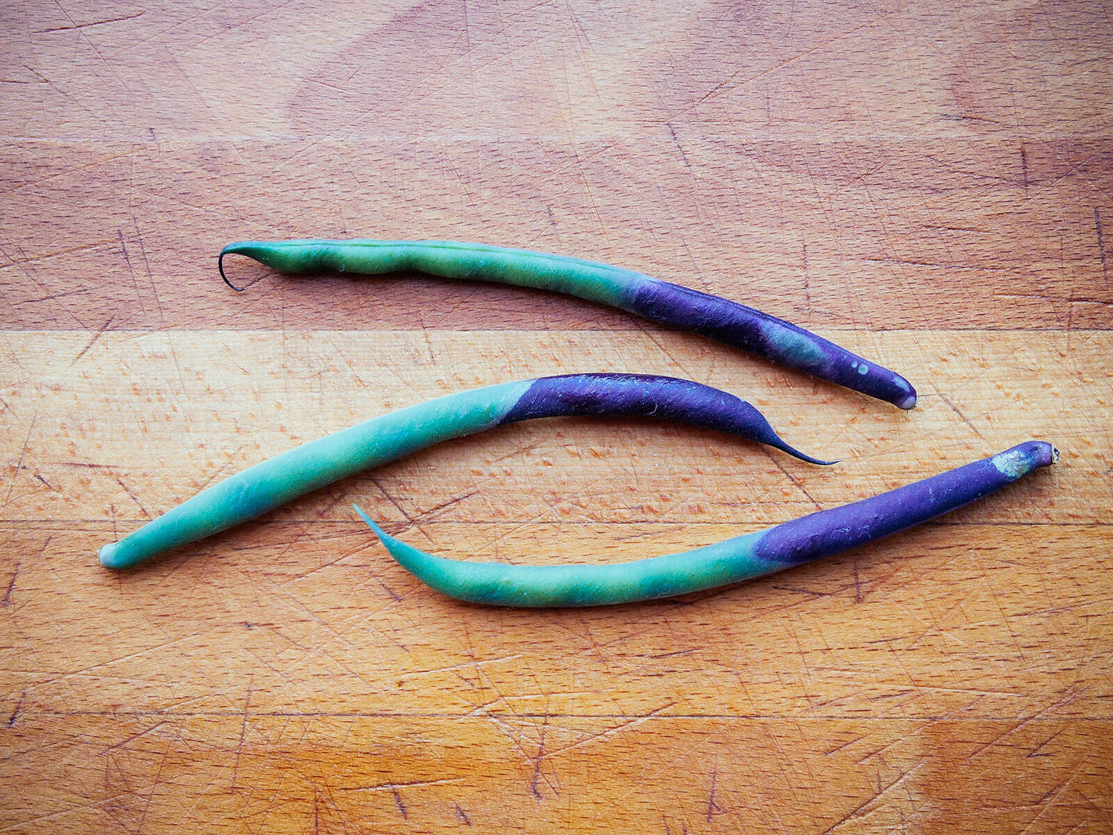 Three beans on a butcher block showing the color shift from purple to green after cooking