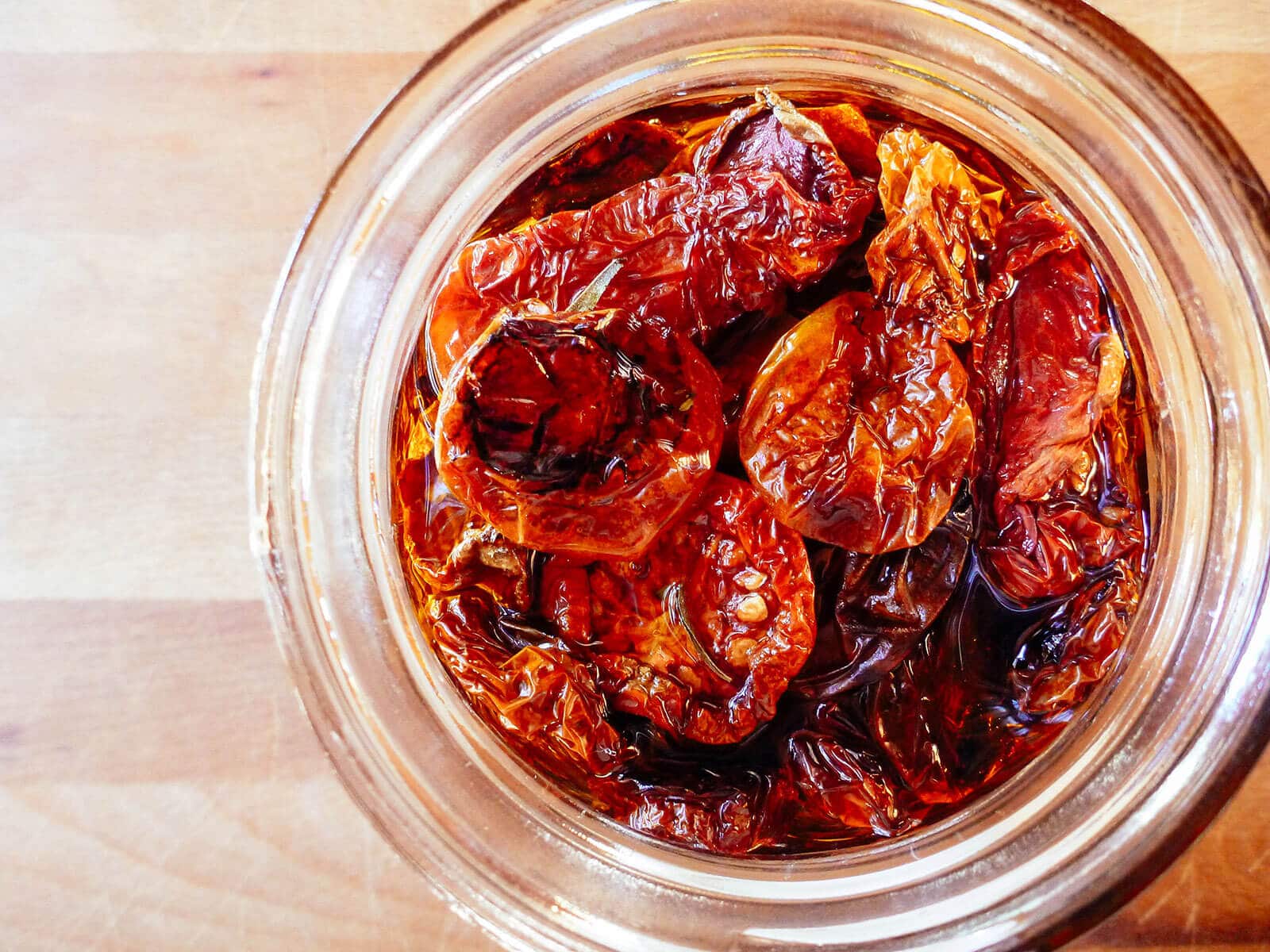 Close-up aerial view of oven-dried tomatoes in olive oil in a glass jar