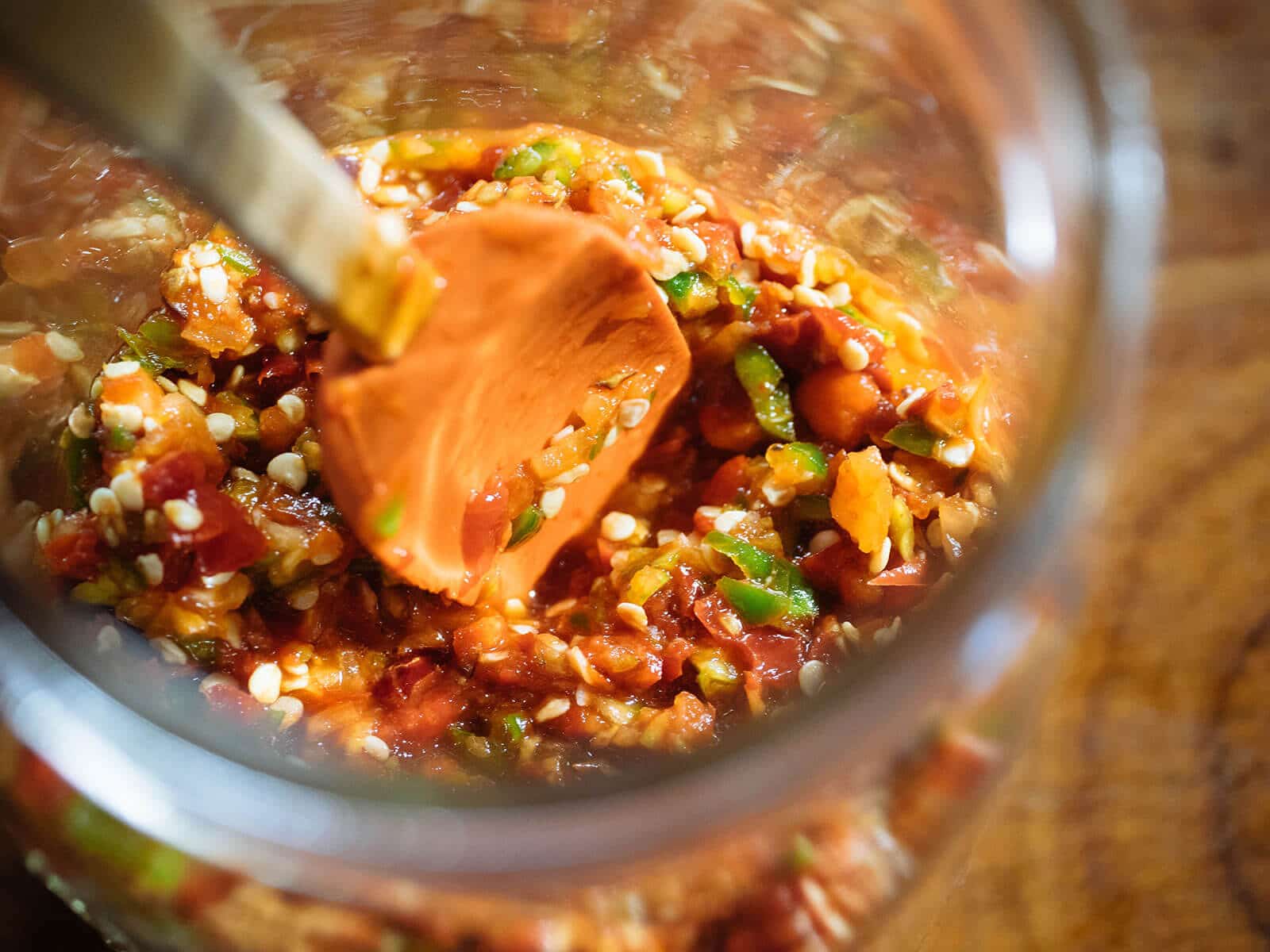 Mini rubber spatula tamping down chile pepper mash in a jar
