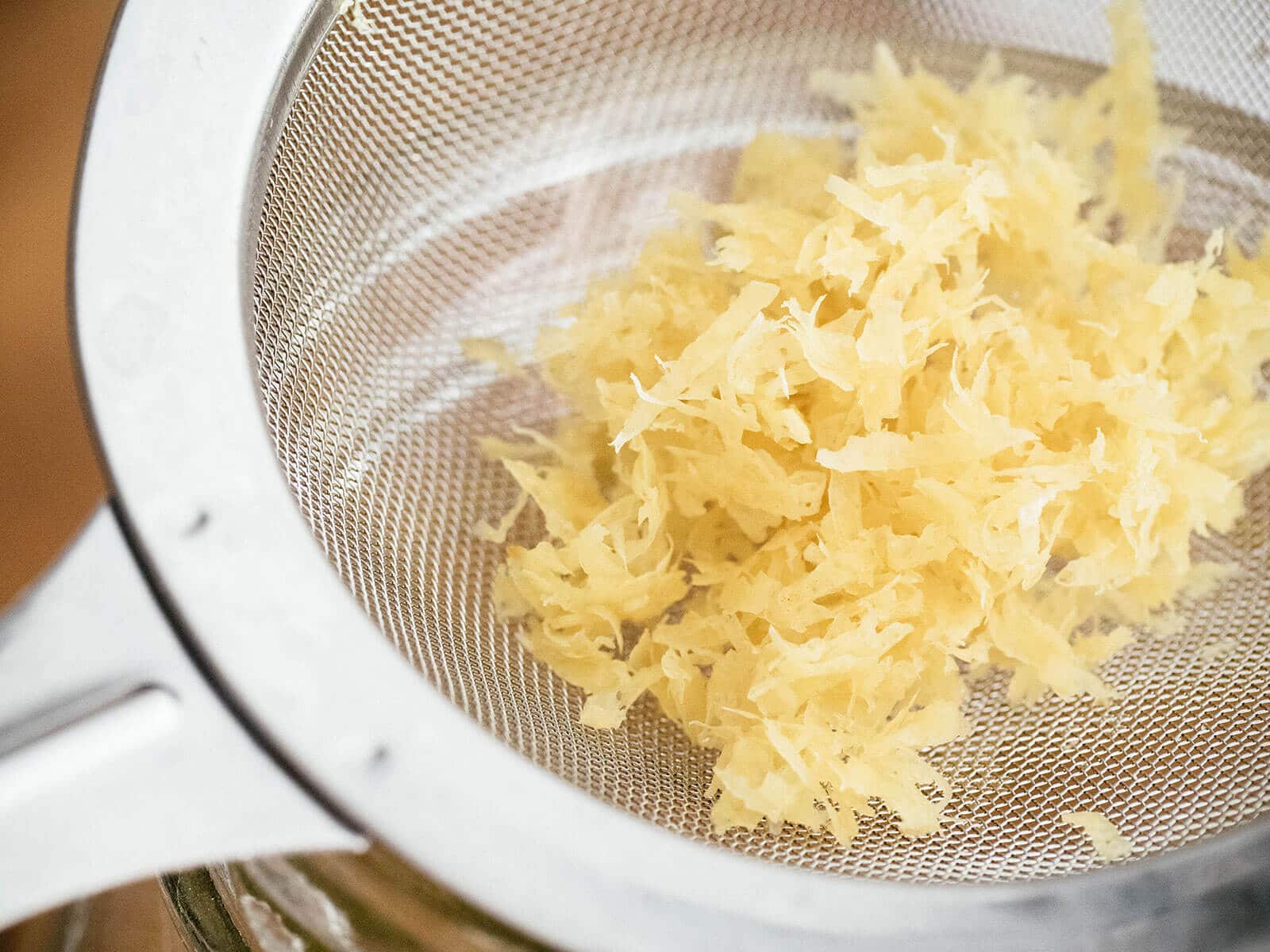 Scoop of pale and brittle lemon zest strained out of a jar