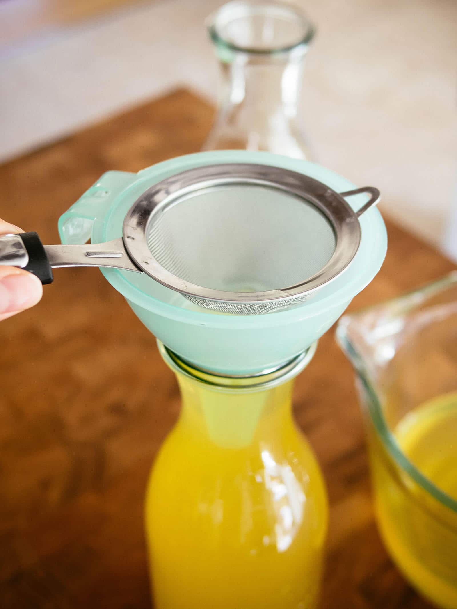 Limoncello being double-strained and funneled into Weck juice jars