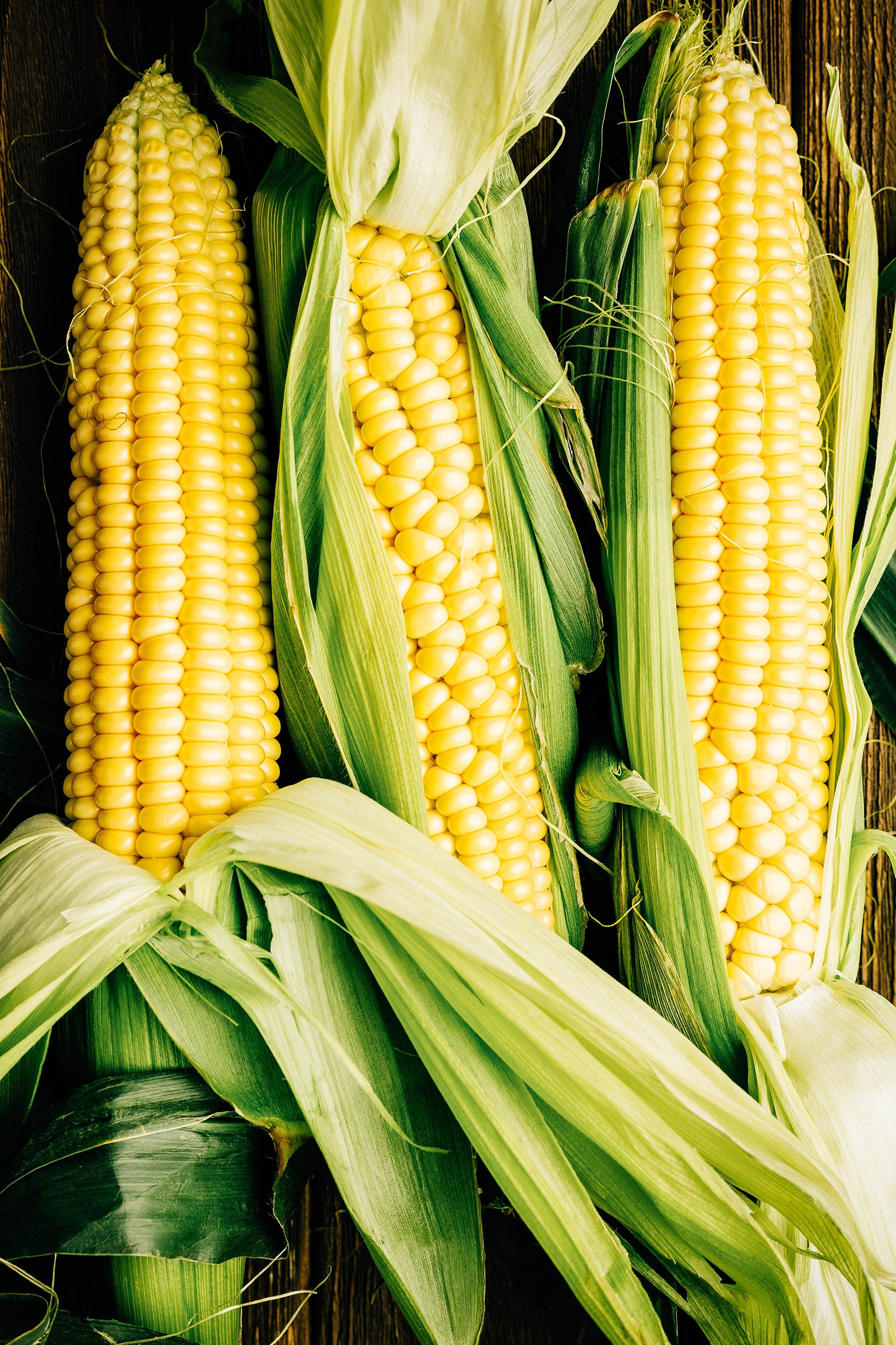 Three ears of corn on a wooden surface