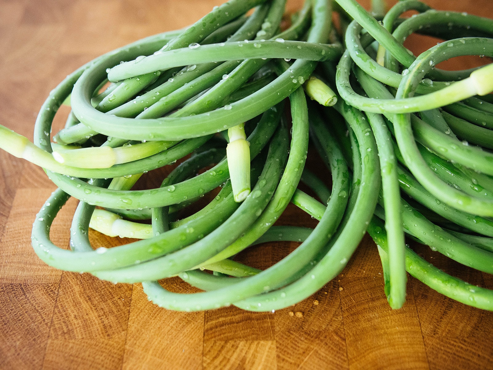 Close-up of garlic scapes washed and piled on a butcher block counter