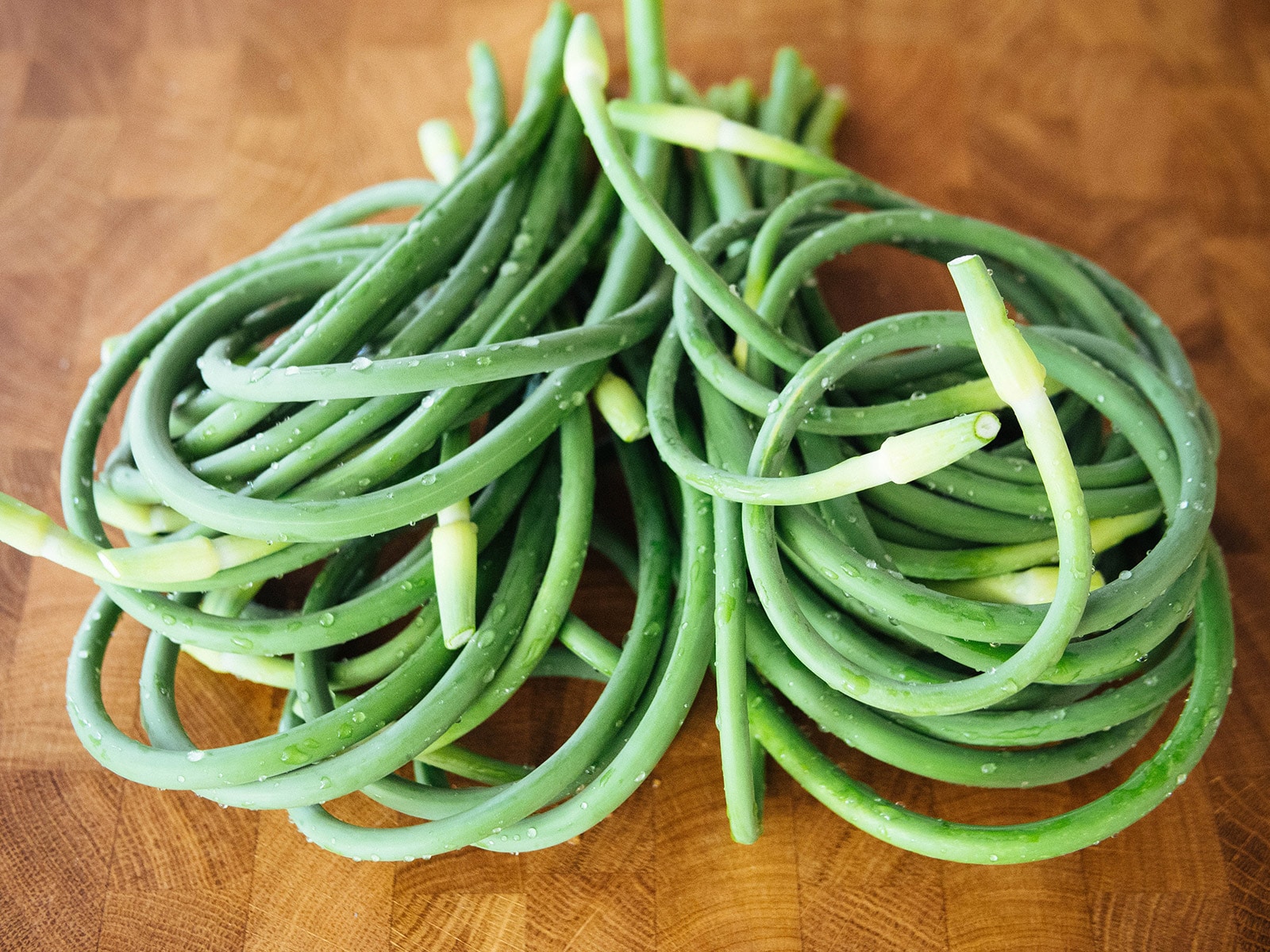 Pile of freshly harvested homegrown garlic scapes on a butcher block counter