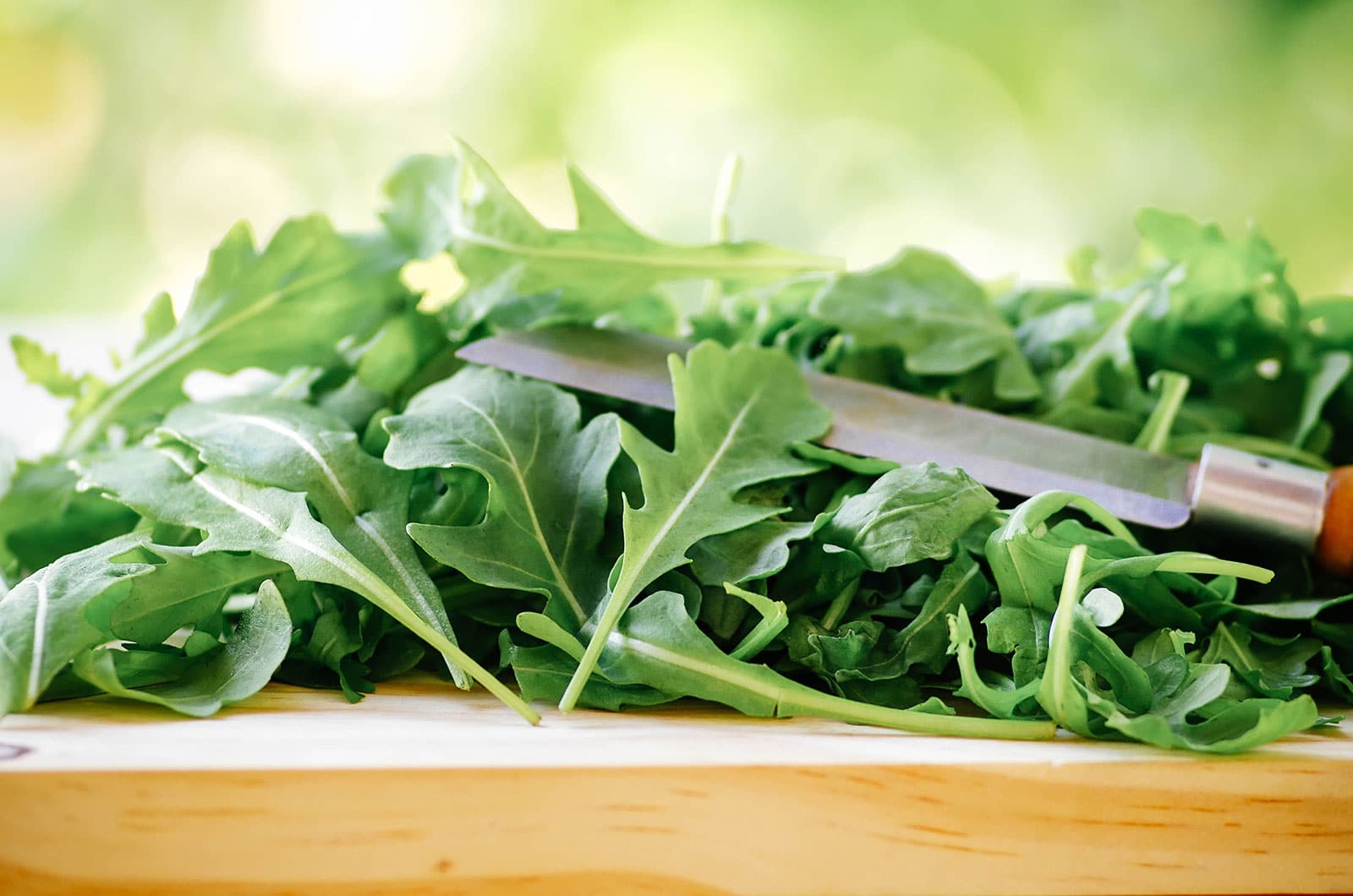 Close-up of baby arugula piled on a cutting board with a knife