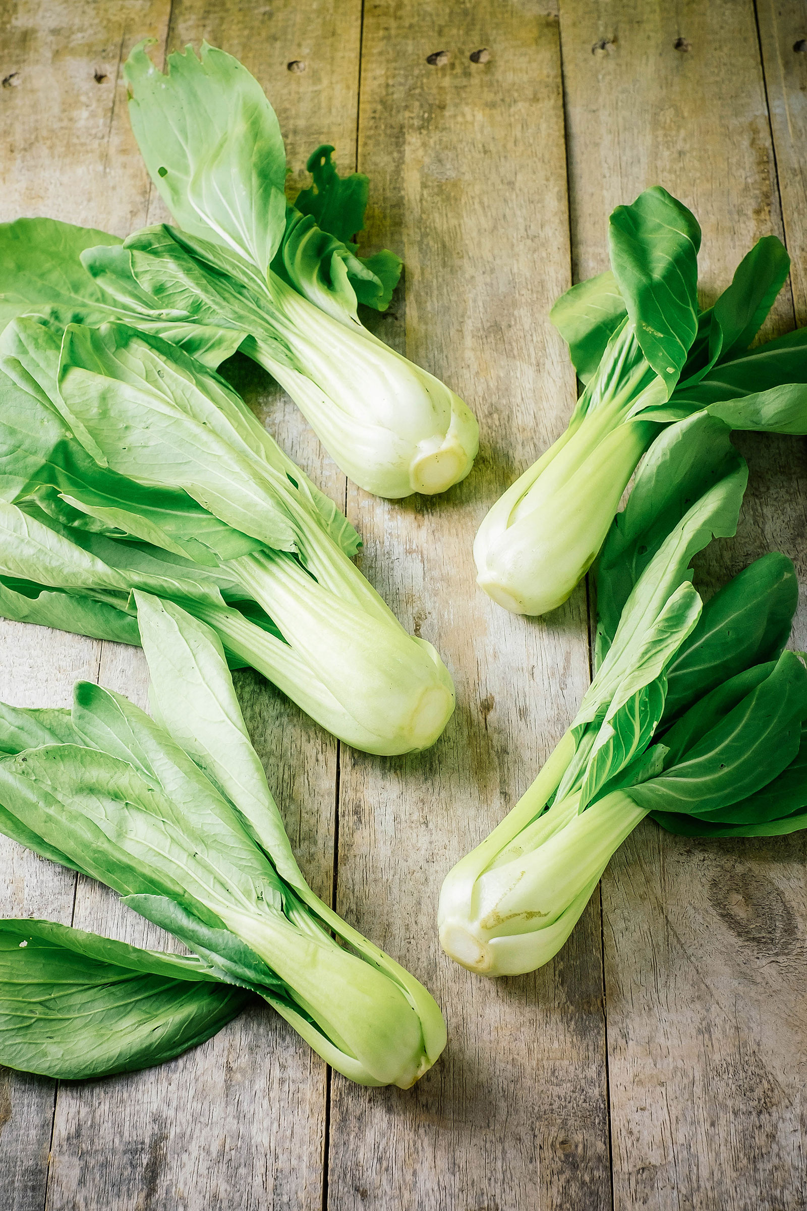 Baby bok choy heads arranged on a rustic wooden surface