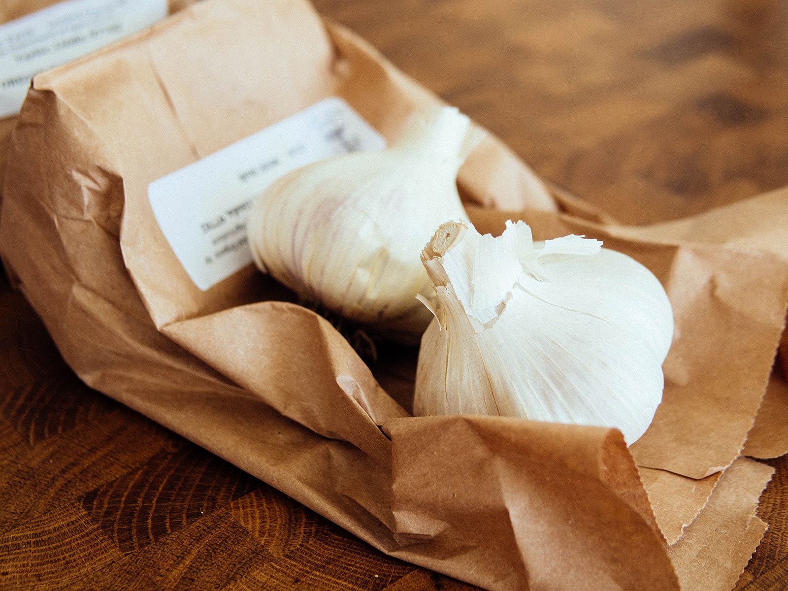 Two bulbs of seed garlic on top of a crumpled brown paper bag