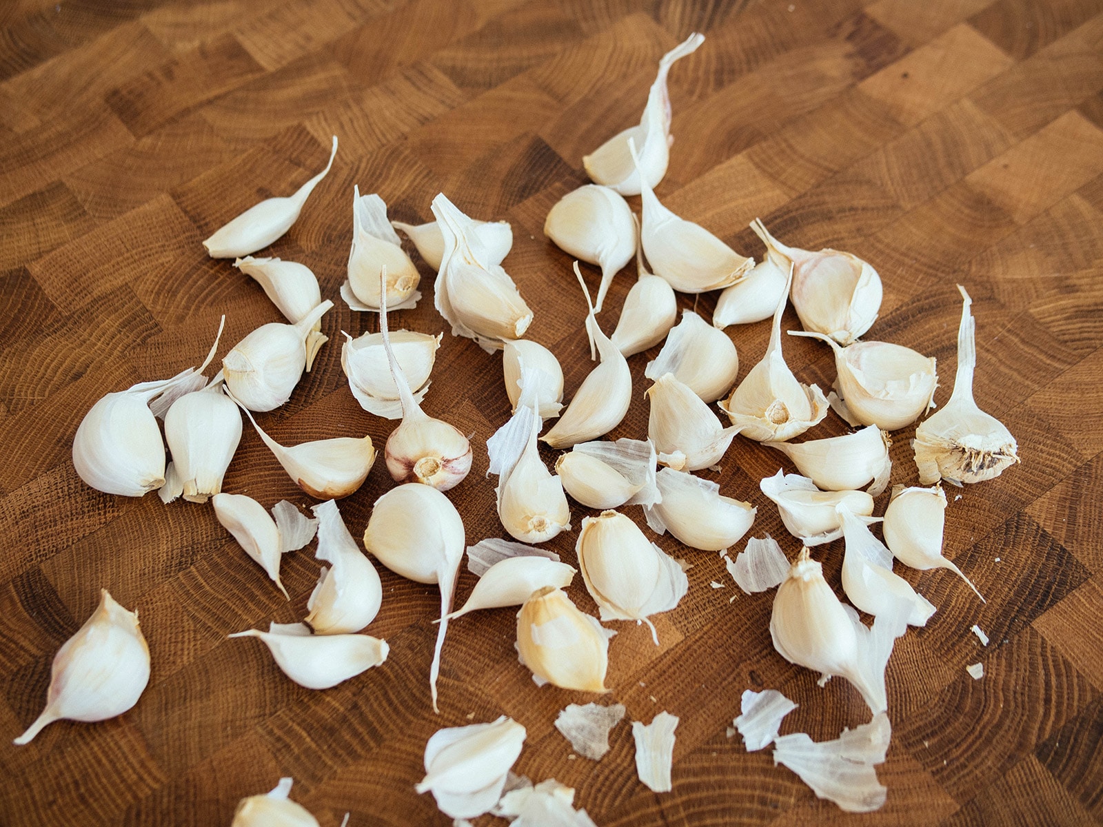 A pile of garlic cloves spread out on a butcher block counter