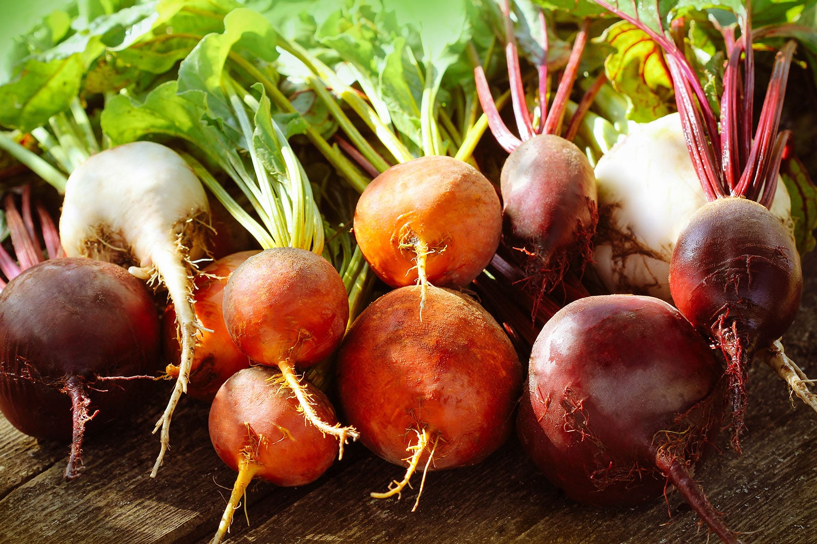 Pile of colorful red, orange, and white beets on a wooden surface