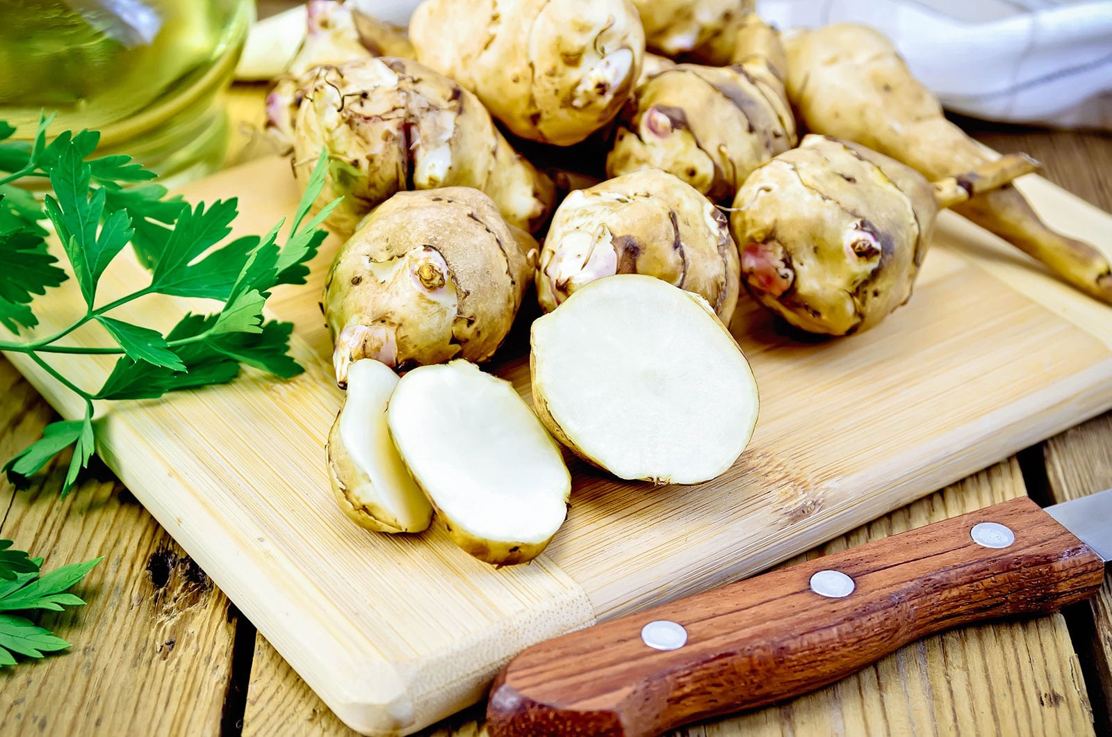 Jerusalem artichokes, whole and sliced, on a cutting board with a knife in the foreground